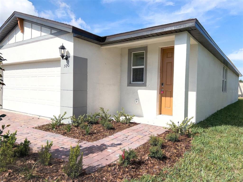 A single-story house with a white stucco exterior, a brown door, and a brick walkway — 590 AMADORAS WAY, ST CLOUD, FL