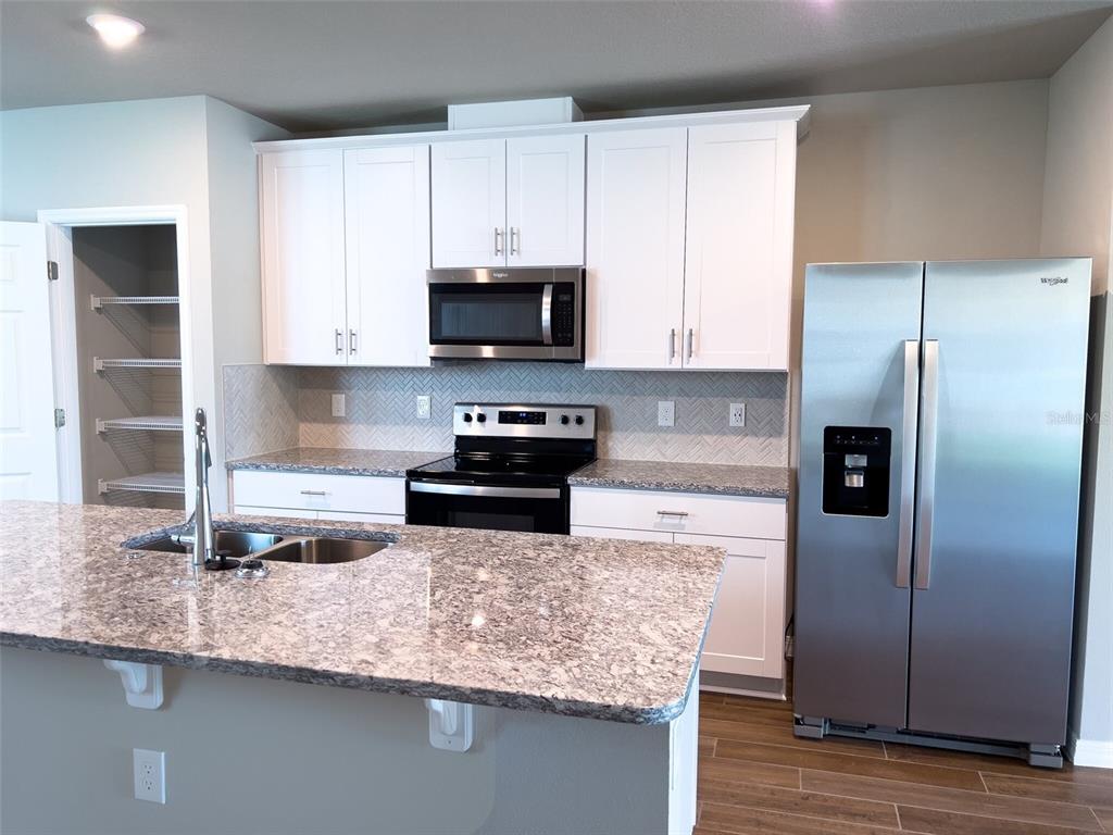 A kitchen features white cabinets, granite countertops, stainless steel appliances, and a central island — 590 AMADORAS WAY, ST CLOUD, FL