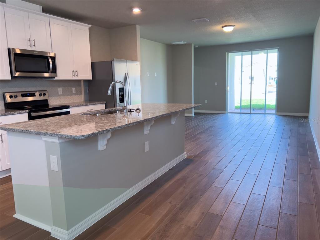 A kitchen with white cabinets, granite countertops, and an island overlooking an open living area — 590 AMADORAS WAY, ST CLOUD, FL