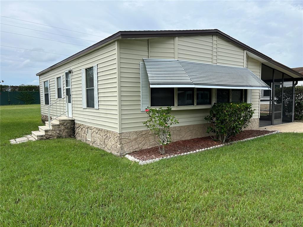 A light-colored manufactured home features horizontal siding, a stone-patterned foundation, and a metal window awning — 120 KENSINGTON PARK DRIVE, DAVENPORT, FL