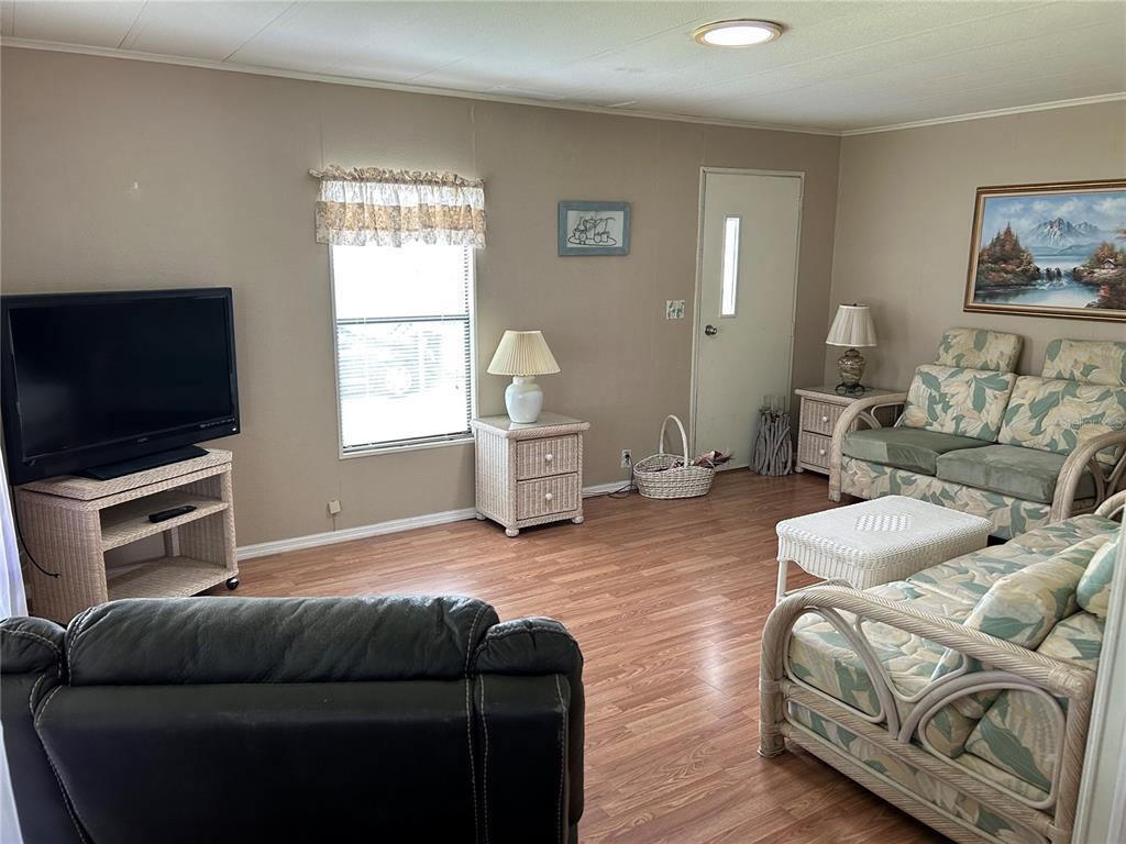 A living room features wood-look flooring, wicker furniture, a television, and a floral sofa — 120 KENSINGTON PARK DRIVE, DAVENPORT, FL