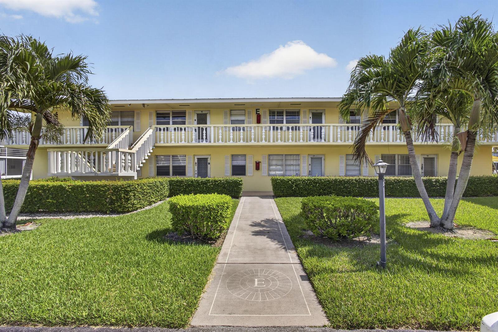 A two-story yellow apartment building features a central walkway, palm trees, and a balcony — 111 Sheffield E, West Palm Beach FL 33417, WEST PALM BEACH, FL