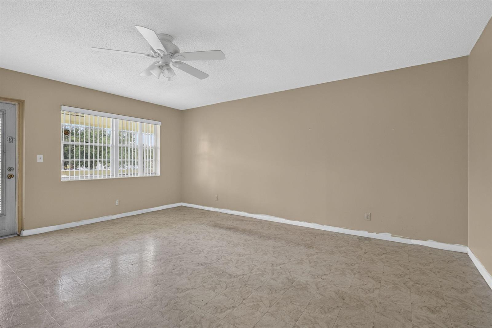 An empty room features beige walls, a white ceiling fan, and light-colored tile flooring — 111 Sheffield E, West Palm Beach FL 33417, WEST PALM BEACH, FL
