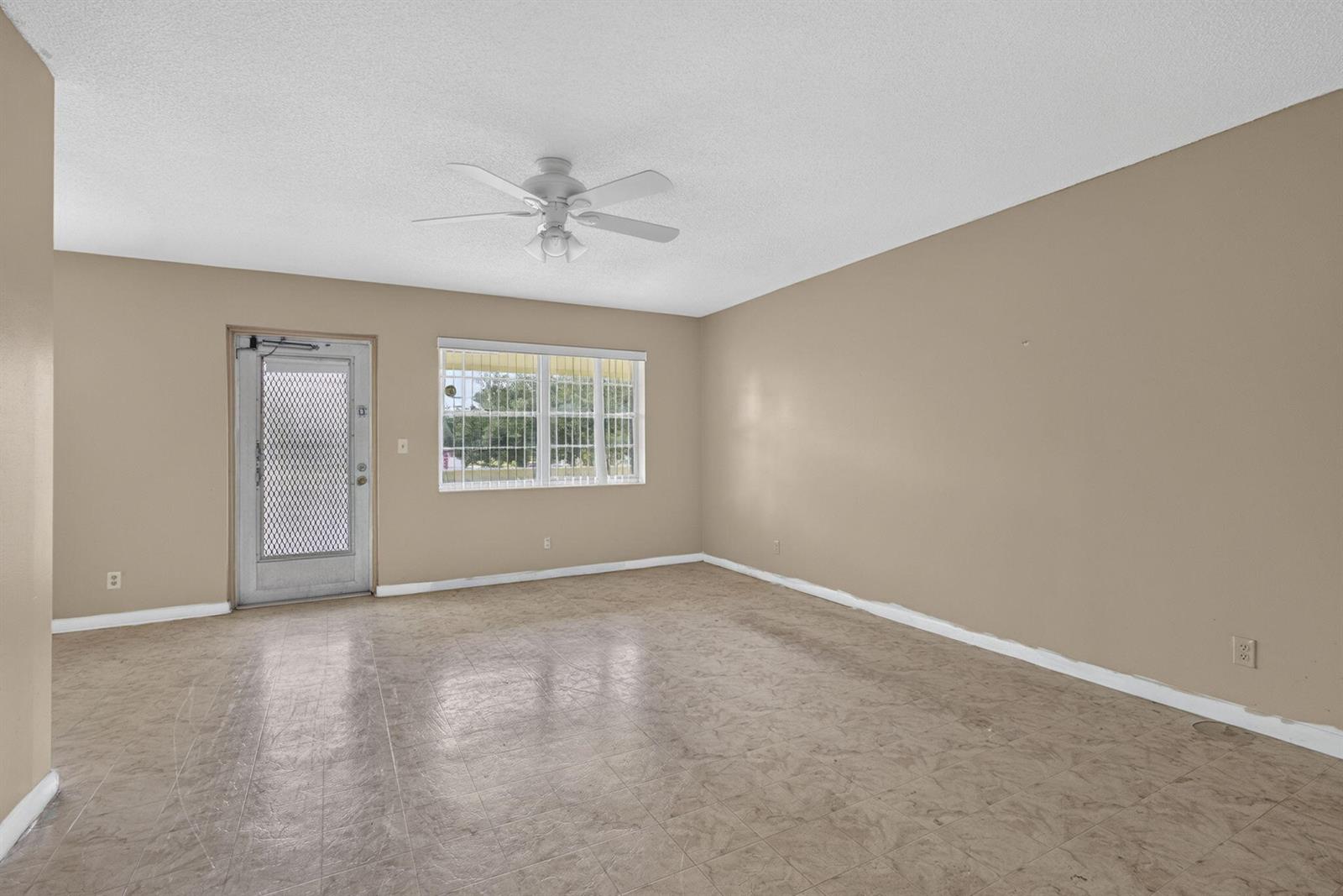 An empty room features tan walls, a ceiling fan, a window, and tiled flooring — 111 Sheffield E, West Palm Beach FL 33417, WEST PALM BEACH, FL