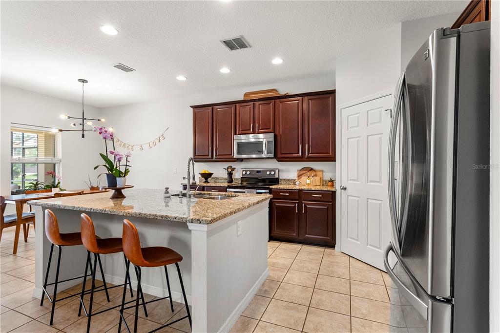 A kitchen features dark wood cabinets, granite countertops, a center island, and stainless steel appliances — 15058 SAWGRASS BLUFF DRIVE, WINTER GARDEN, FL