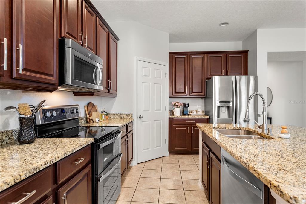 A kitchen features dark wood cabinets, granite countertops, stainless steel appliances, and tile flooring — 15058 SAWGRASS BLUFF DRIVE, WINTER GARDEN, FL