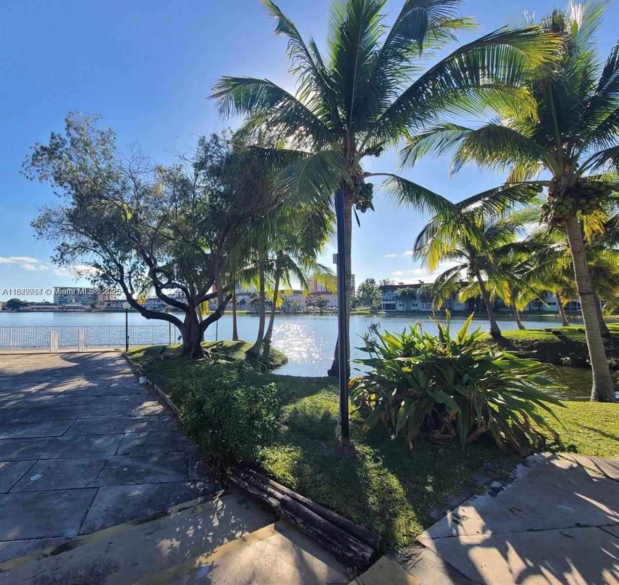 A paved walkway leads to a grassy area with palm trees overlooking a lake — 1450 NE 191st St # 404, Miami FL 33179, MIAMI, FL