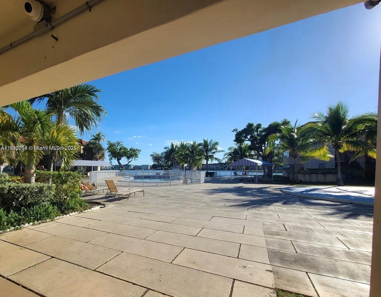 A patio overlooks a swimming pool area with palm trees and a waterfront view — 1450 NE 191st St # 404, Miami FL 33179, MIAMI, FL