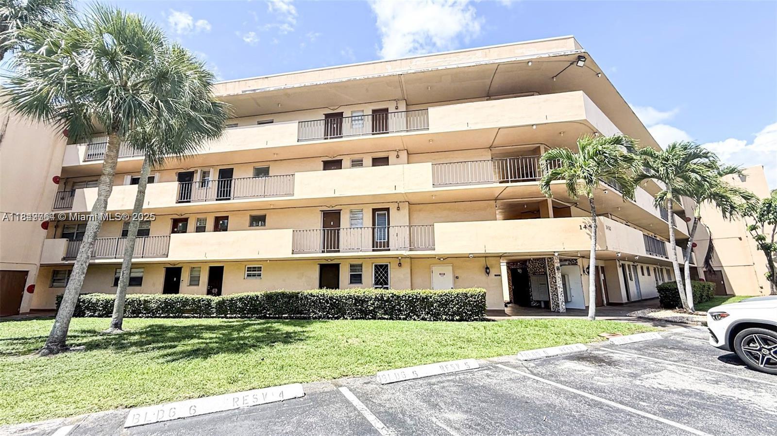 A three-story apartment building features exterior walkways, balconies, and a paved parking lot in front — 1450 NE 191st St # 404, Miami FL 33179, MIAMI, FL