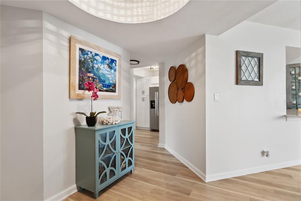 A hallway features light wood flooring, a blue cabinet, and wall art leading toward a kitchen — 5279 ISLA KEY BOULEVARD S UNIT 212, ST PETERSBURG, FL