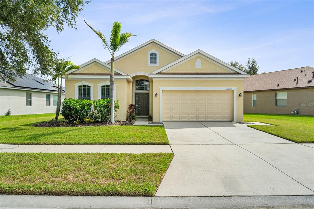A single-story yellow stucco house with a two-car garage and a palm tree — 12720 WHITNEY MEADOW WAY, RIVERVIEW, FL