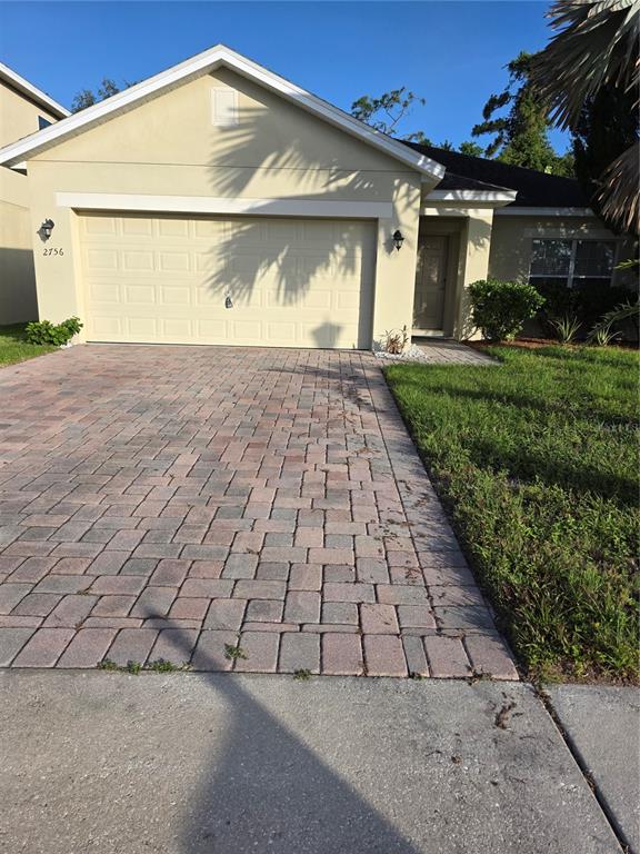 A single-story house with a beige stucco exterior, a two-car garage, and a paver driveway — 2756 BIG TIMBER DRIVE, KISSIMMEE, FL