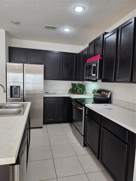 A kitchen features dark wood cabinets, stainless steel appliances, and light-colored countertops — 2756 BIG TIMBER DRIVE, KISSIMMEE, FL