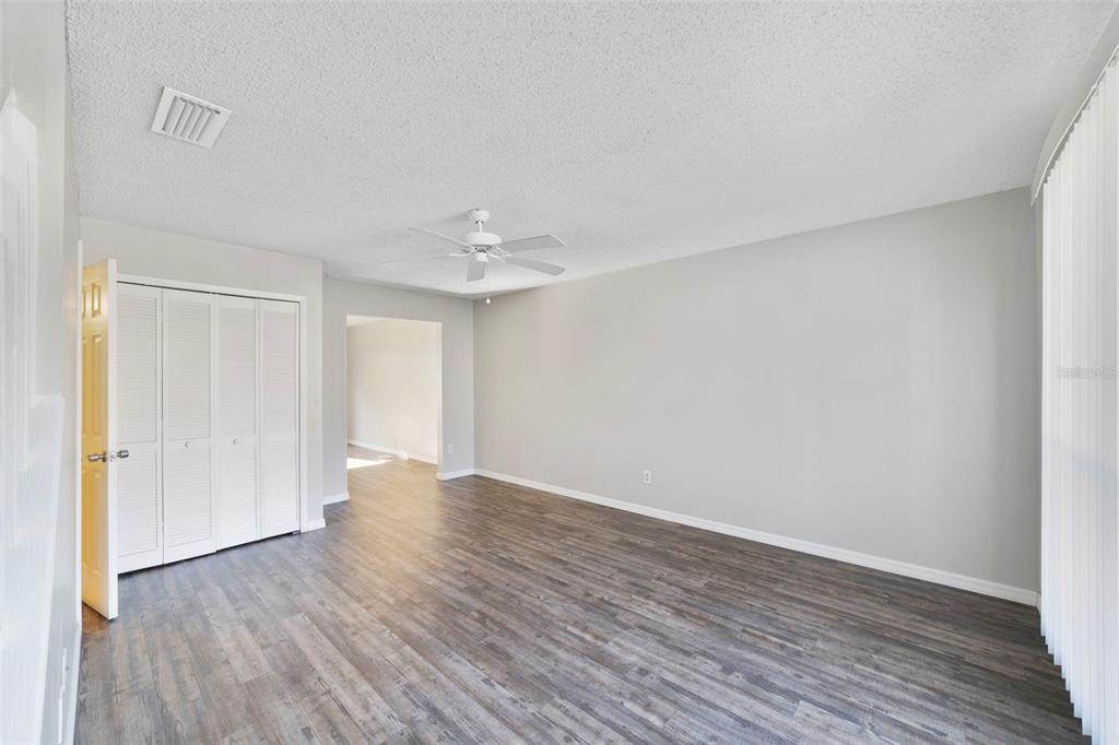 An empty room features gray walls, wood-look flooring, a ceiling fan, and white closet doors — 605 CASA PARK COURT UNIT H, WINTER SPRINGS, FL