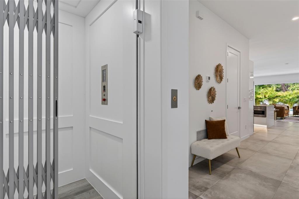 A white elevator with a metal gate stands next to a hallway with a bench — 1671 ARLINGTON STREET, SARASOTA, FL