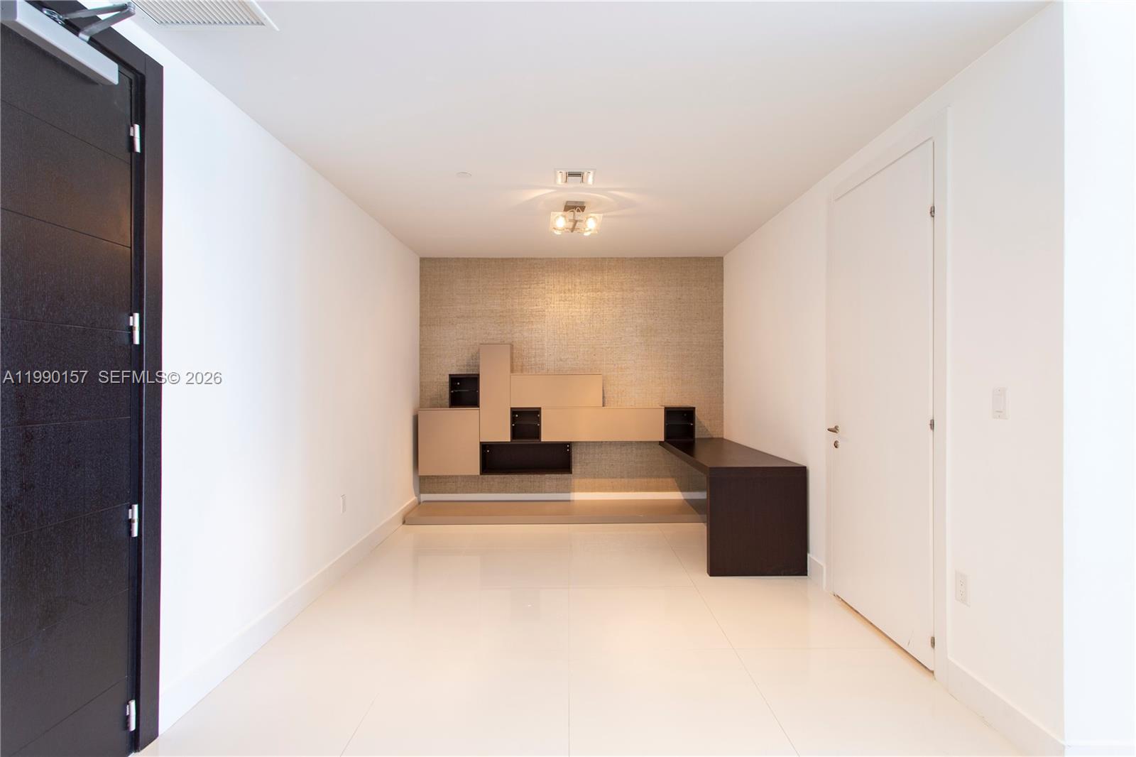 A modern room features white tile flooring, a textured accent wall, and built-in shelving — 200 BISCAYNE BLVD WY # 4512, Miami FL 33131, MIAMI, FL