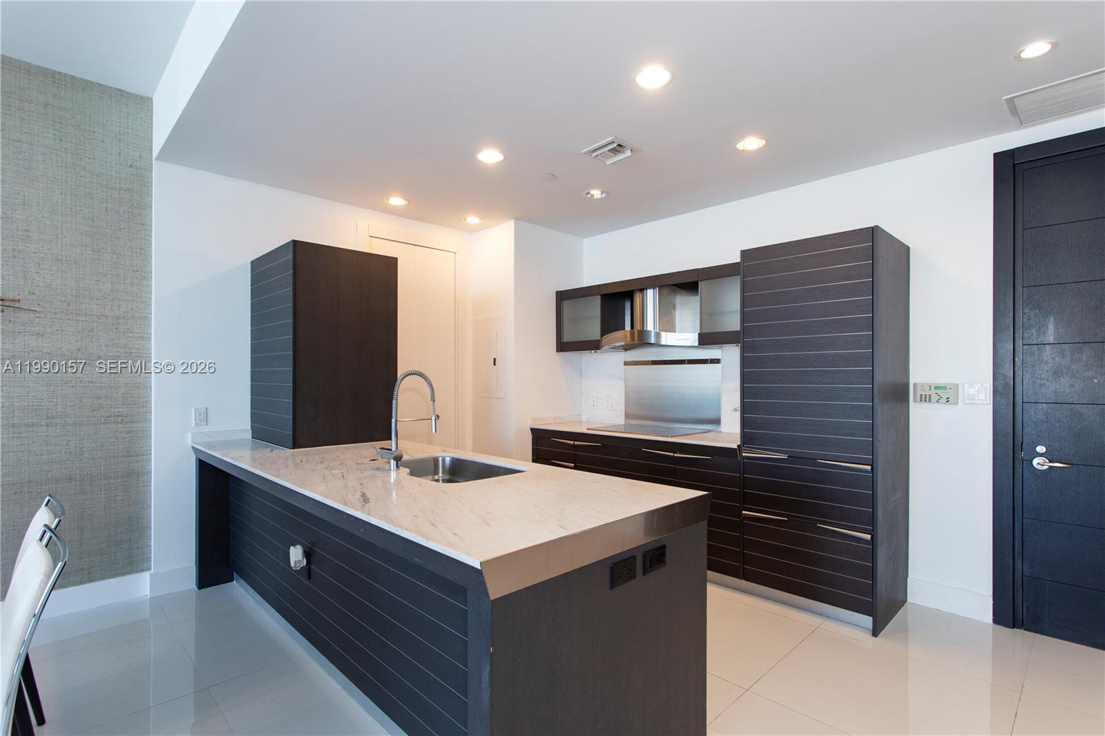 A modern kitchen features dark wood cabinetry, a marble-topped island with a sink, and tile flooring — 200 BISCAYNE BLVD WY # 4512, Miami FL 33131, MIAMI, FL