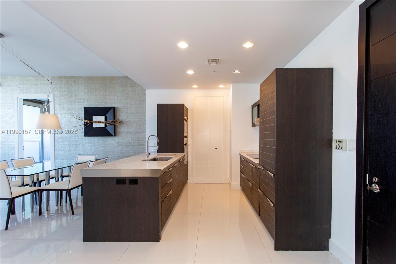 A modern kitchen features dark wood cabinetry, stainless steel countertops, and white tile flooring — 200 BISCAYNE BLVD WY # 4512, Miami FL 33131, MIAMI, FL
