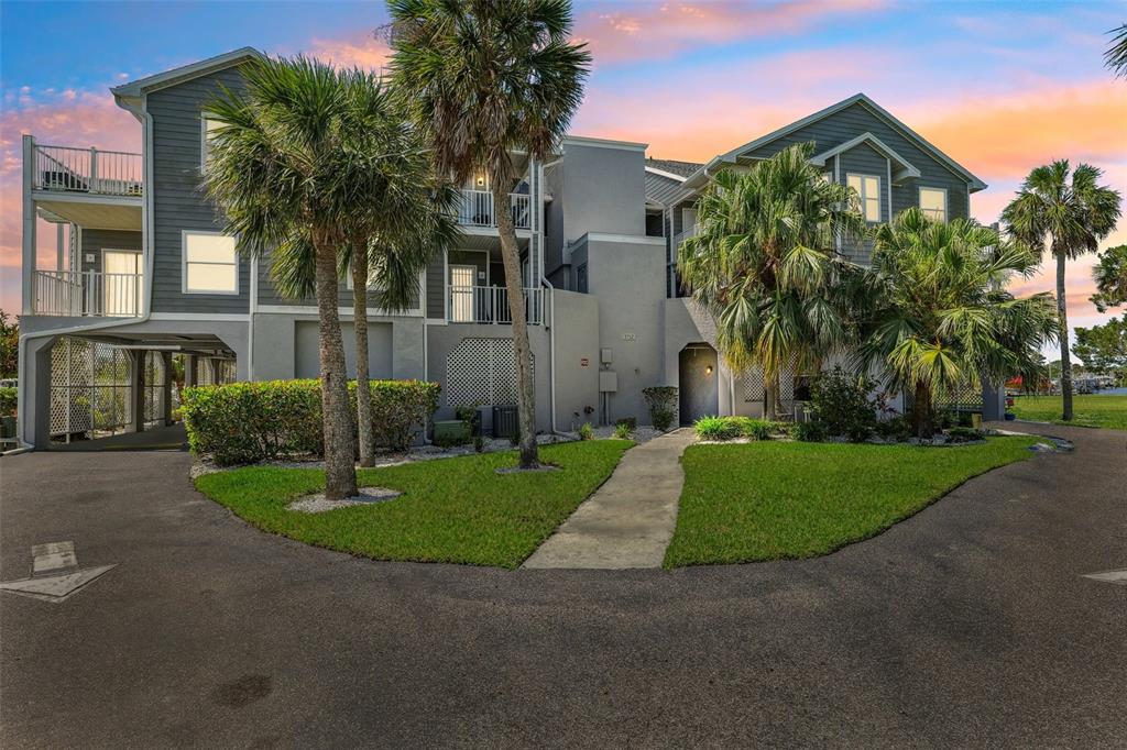 A multi-story residential building with gray siding, balconies, and palm trees under a sunset sky — 5712 BISCAYNE COURT UNIT 103, NEW PORT RICHEY, FL