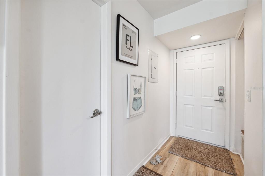 A white entry door leads into a small hallway with light wood flooring and wall art — 5712 BISCAYNE COURT UNIT 103, NEW PORT RICHEY, FL