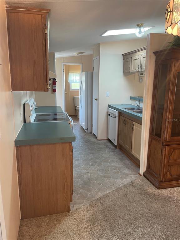 A kitchen with wood cabinets, green countertops, and a white refrigerator leads to a bathroom — 29168 CRAWFORD AVENUE, PUNTA GORDA, FL