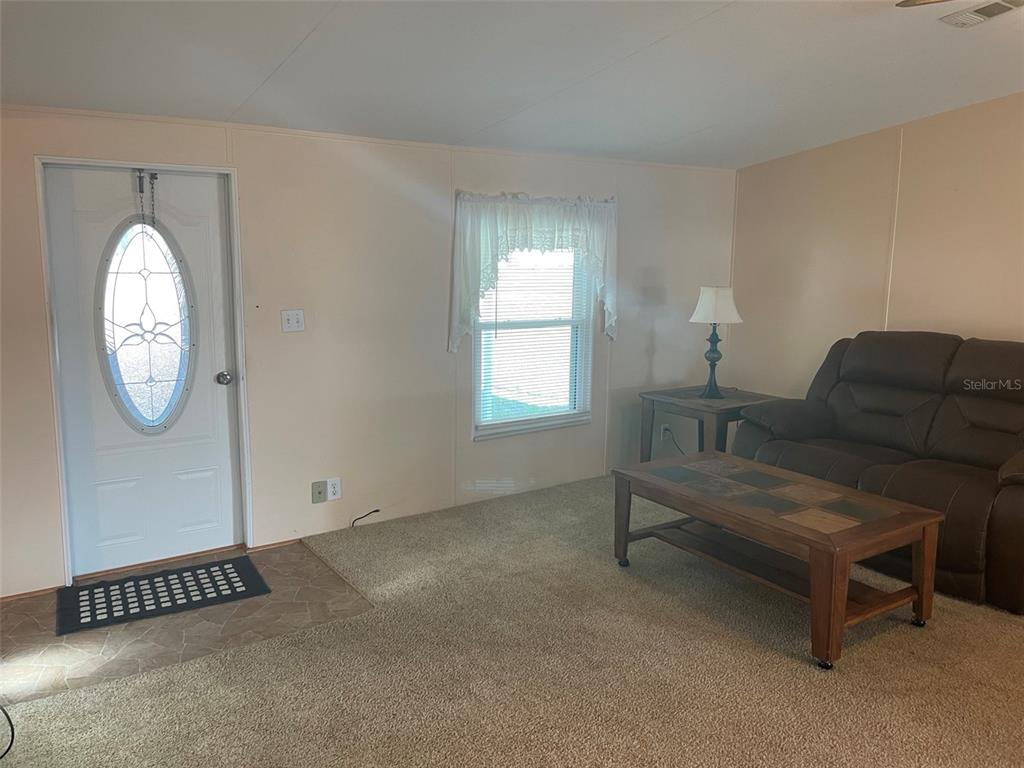 A living room features beige walls, carpeted flooring, a front door, and a brown sofa — 29168 CRAWFORD AVENUE, PUNTA GORDA, FL