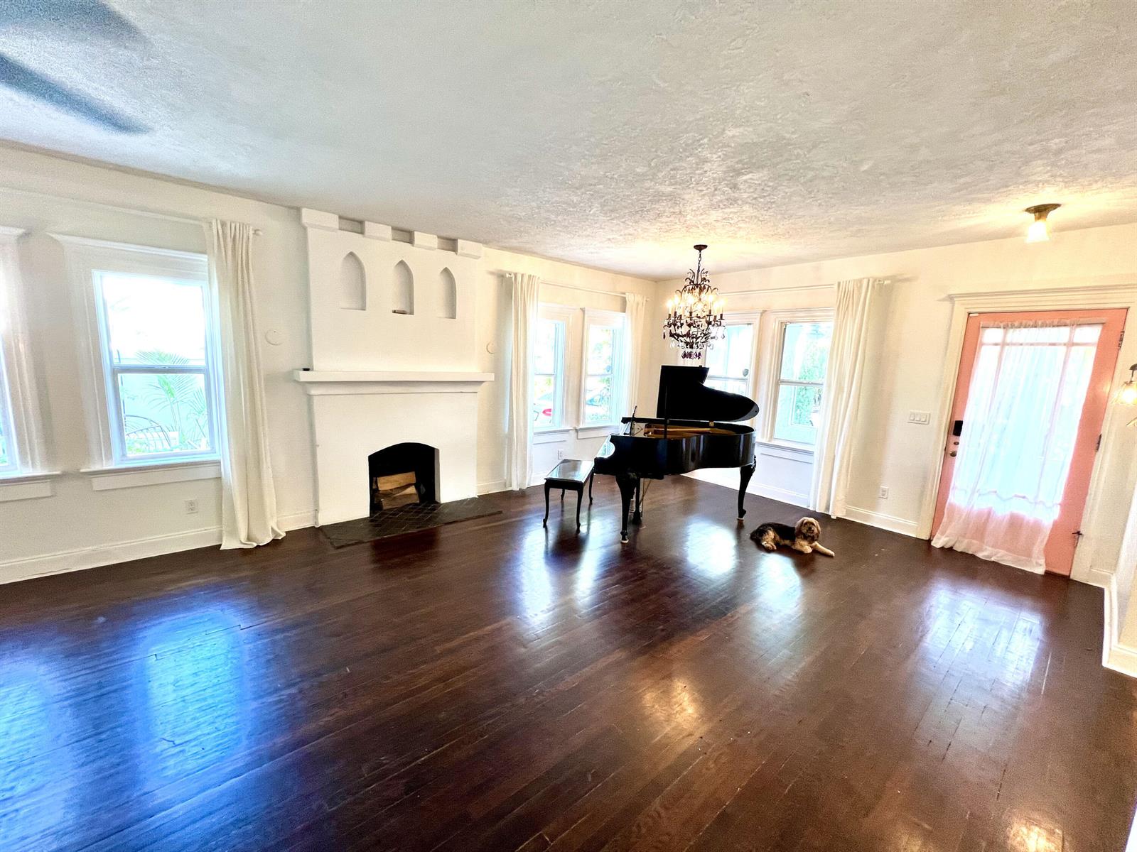 A spacious living room features dark hardwood floors, a white fireplace, and a grand piano — 312 Fordham Drive, Lake Worth FL 33460, LAKE WORTH, FL