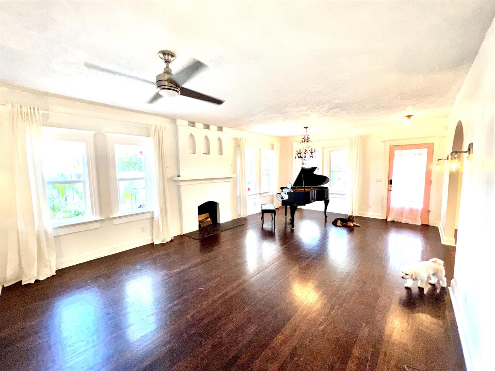 A spacious living room features dark hardwood floors, a white fireplace, and a grand piano — 312 Fordham Drive, Lake Worth FL 33460, LAKE WORTH, FL