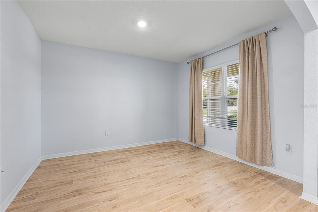 An empty bedroom features light-colored walls, wood-look flooring, and a window with beige curtains — 2731 FIELDBROOKE WAY, EDGEWATER, FL