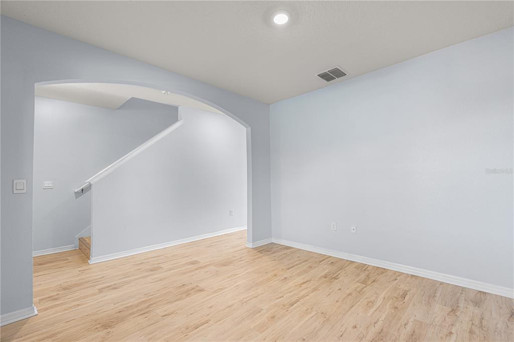 An empty room with light wood-look flooring, light blue walls, and an arched entryway — 2731 FIELDBROOKE WAY, EDGEWATER, FL