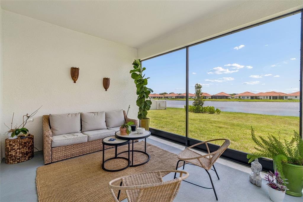 A screened-in patio features a wicker sofa, two chairs, and a view of a lake — 17307 BLUE WALK STREET, WIMAUMA, FL