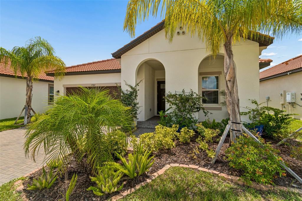 The exterior of a single-story house features a tiled roof, arched entryway, and palm trees — 17307 BLUE WALK STREET, WIMAUMA, FL