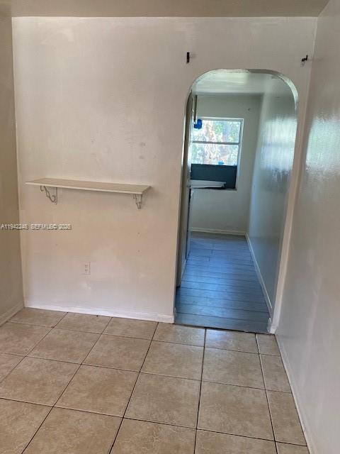 A room with beige tile flooring and a wall-mounted shelf leads through an arched doorway — 100 SE 3 Ave # 3, Hallandale Beach FL 33009, HALLANDALE BEACH, FL