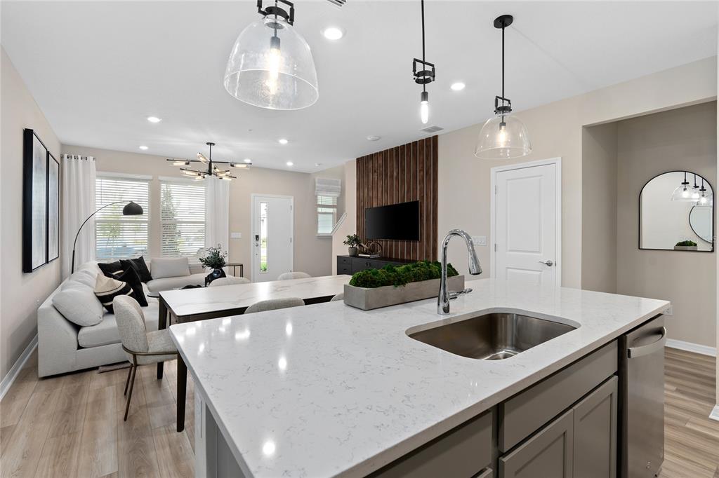 A kitchen island with a quartz countertop overlooks an open-concept living and dining area — 10690 EVENING STAR STREET, ORLANDO, FL