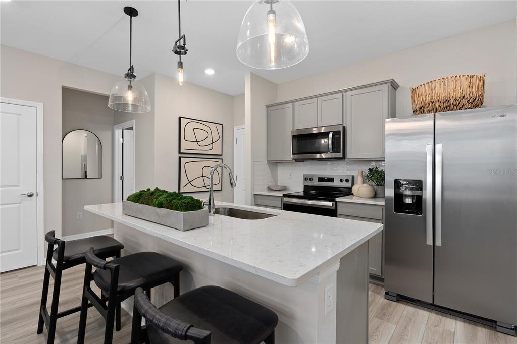 A modern kitchen features gray cabinets, stainless steel appliances, and a white quartz island — 10690 EVENING STAR STREET, ORLANDO, FL