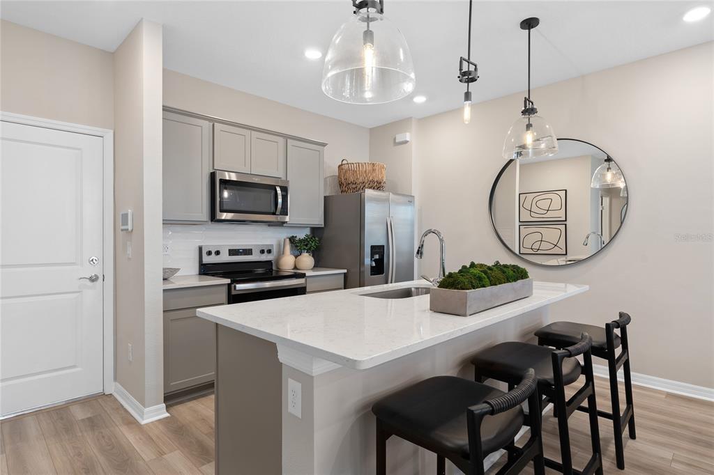 A kitchen features gray cabinets, white quartz countertops, a center island, and three bar stools — 10690 EVENING STAR STREET, ORLANDO, FL