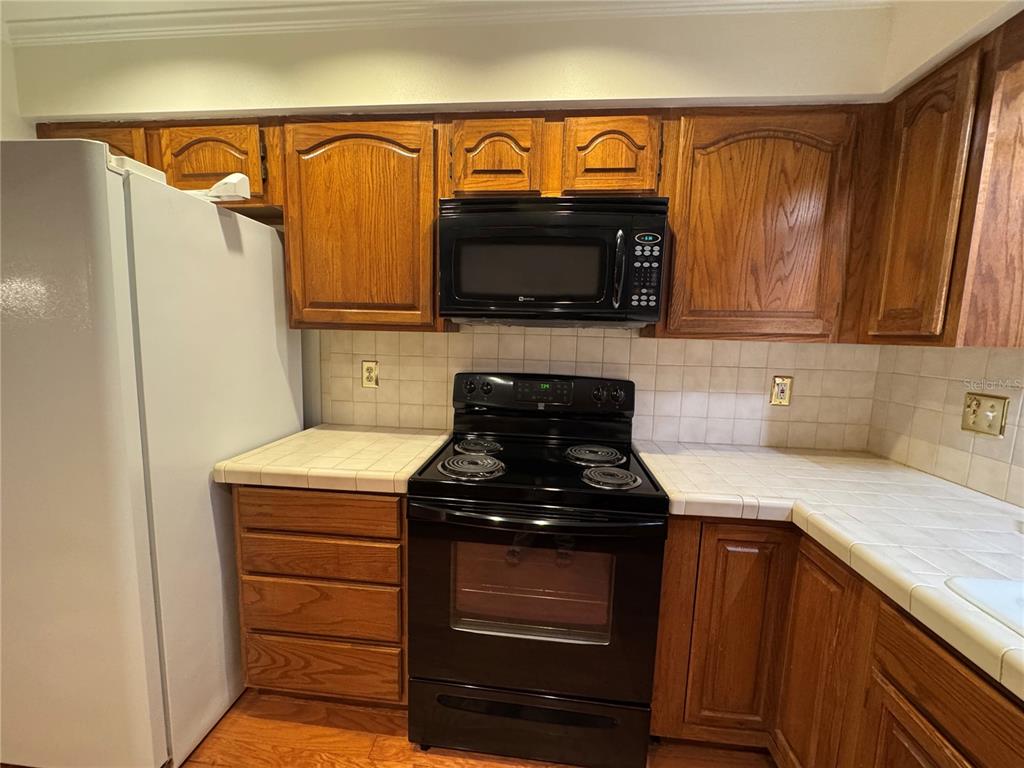 A kitchen features oak cabinets, a black stove and microwave, and white tile countertops — 10 FT CLINCH HEIGHTS ROAD, FROSTPROOF, FL