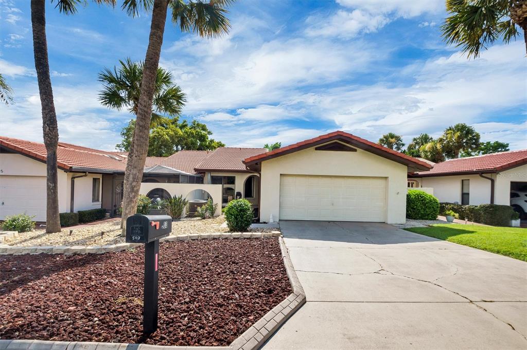 A single-story house with a tiled roof, two-car garage, and palm trees at sunset — 503 CLUBHOUSE DRIVE, LAKE WALES, FL