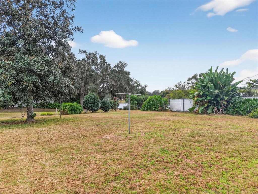 A grassy backyard features a metal-roofed carport and a house with a screened-in porch — XXXX S INDIANA AVENUE, GROVELAND, FL