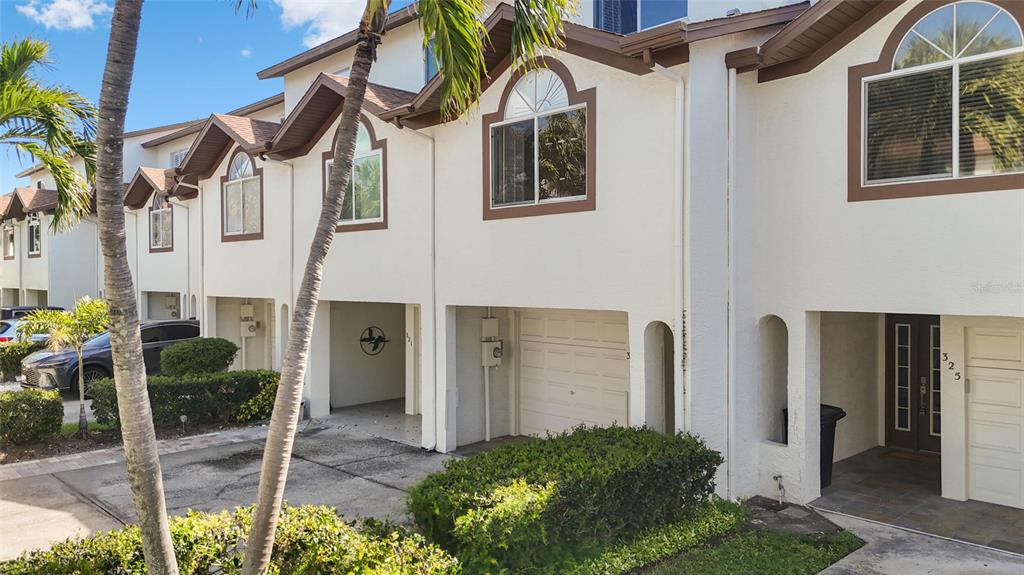 A row of white townhouses with arched windows, garages, and palm trees in the foreground — 323 MADEIRA CIRCLE, ST PETERSBURG, FL