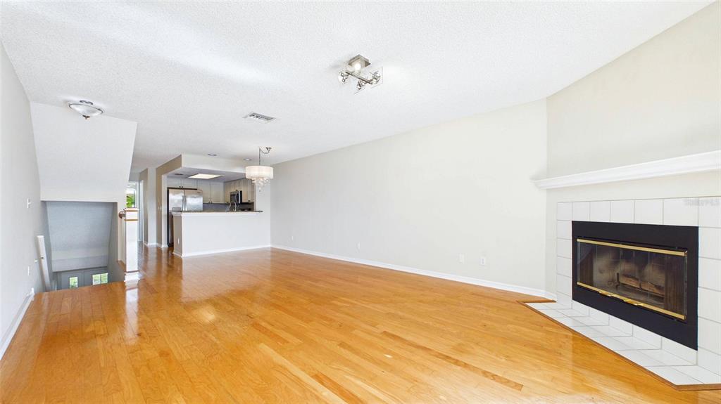 A living room with hardwood floors, a fireplace, and an open kitchen in the background — 323 MADEIRA CIRCLE, ST PETERSBURG, FL