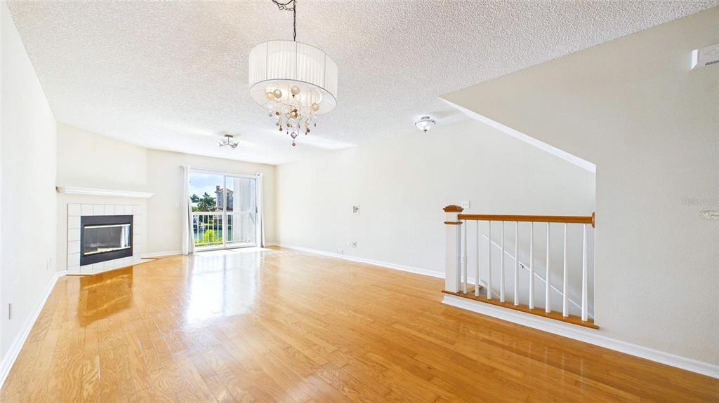 A living room features hardwood floors, a corner fireplace, a chandelier, and a staircase railing — 323 MADEIRA CIRCLE, ST PETERSBURG, FL