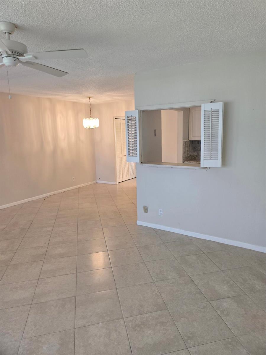 An open-concept living area with tile flooring, a ceiling fan, and a kitchen pass-through window — 99 Salisbury E, West Palm Beach FL 33417, WEST PALM BEACH, FL