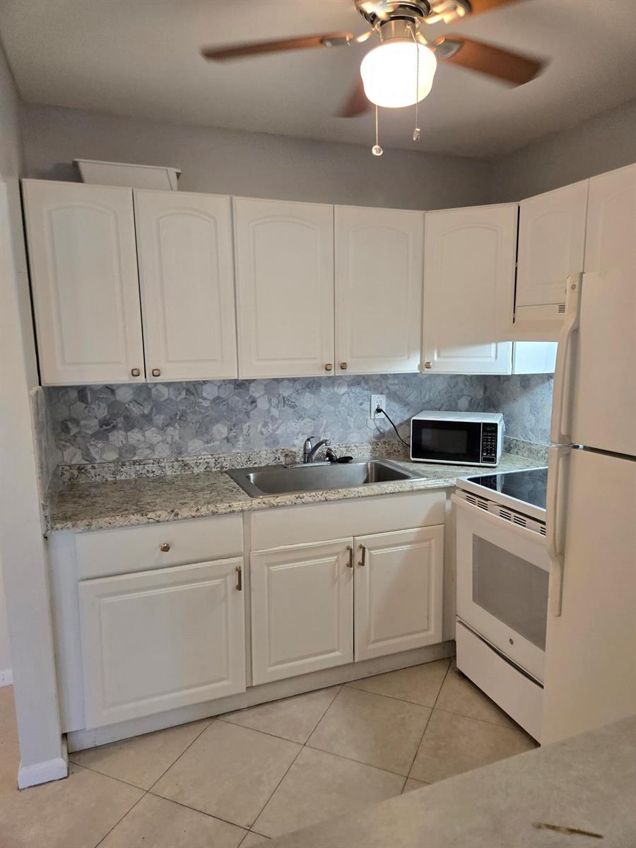 A kitchen with white cabinets, granite countertops, a hexagonal tile backsplash, and white appliances — 99 Salisbury E, West Palm Beach FL 33417, WEST PALM BEACH, FL