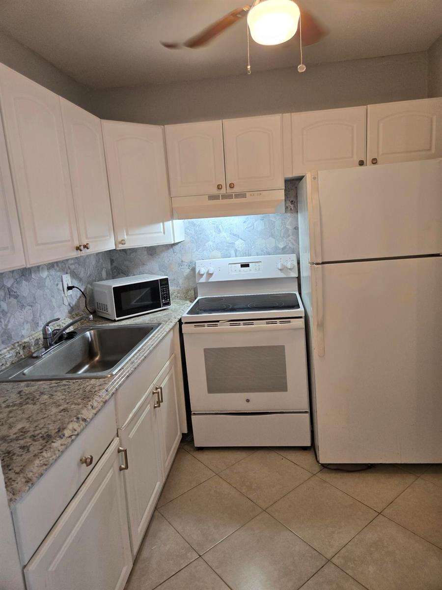 A kitchen features white cabinets, a white stove, a white refrigerator, and a tiled backsplash — 99 Salisbury E, West Palm Beach FL 33417, WEST PALM BEACH, FL