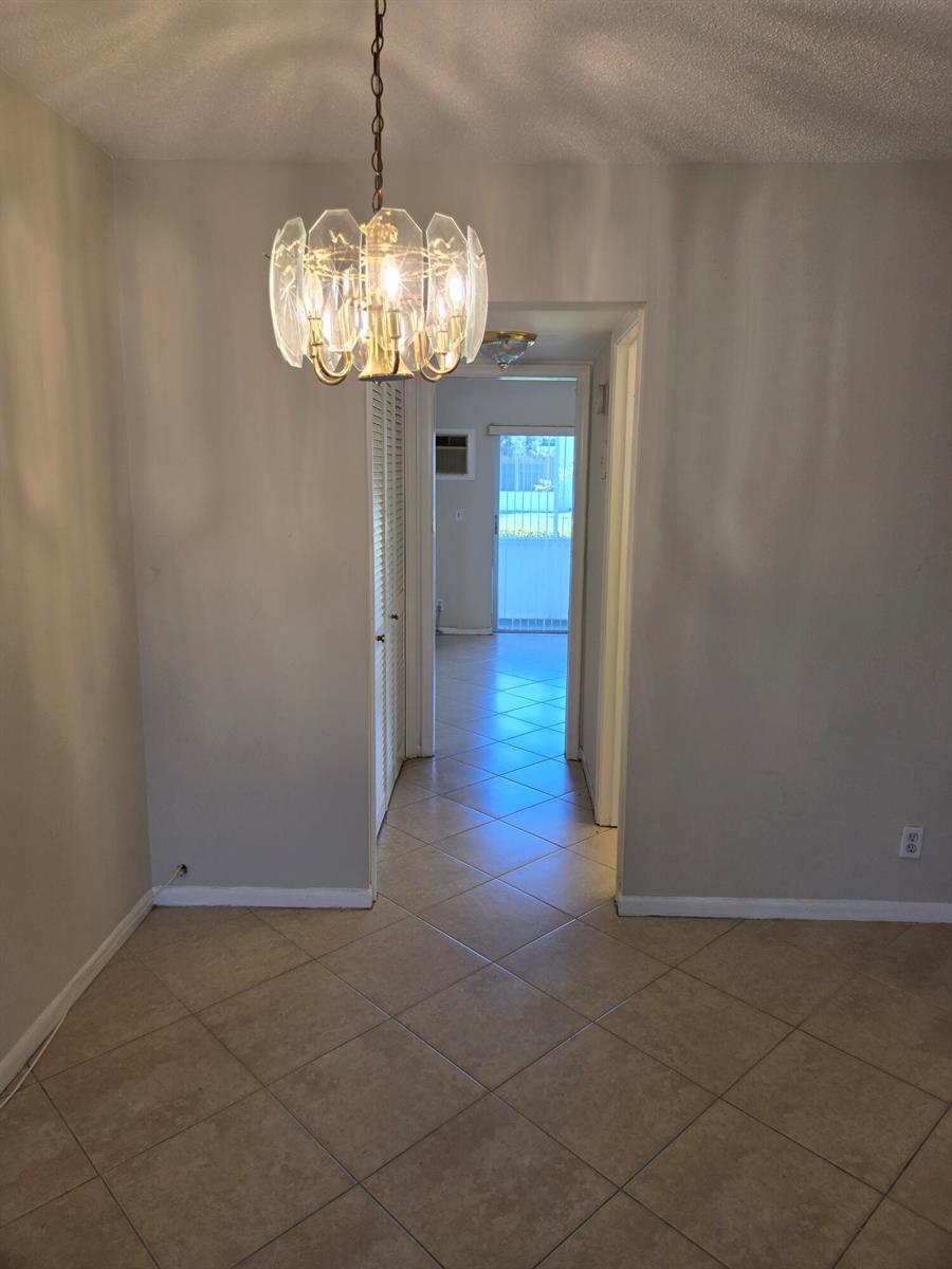 A dining area with a crystal chandelier and tile flooring leads into a hallway — 99 Salisbury E, West Palm Beach FL 33417, WEST PALM BEACH, FL