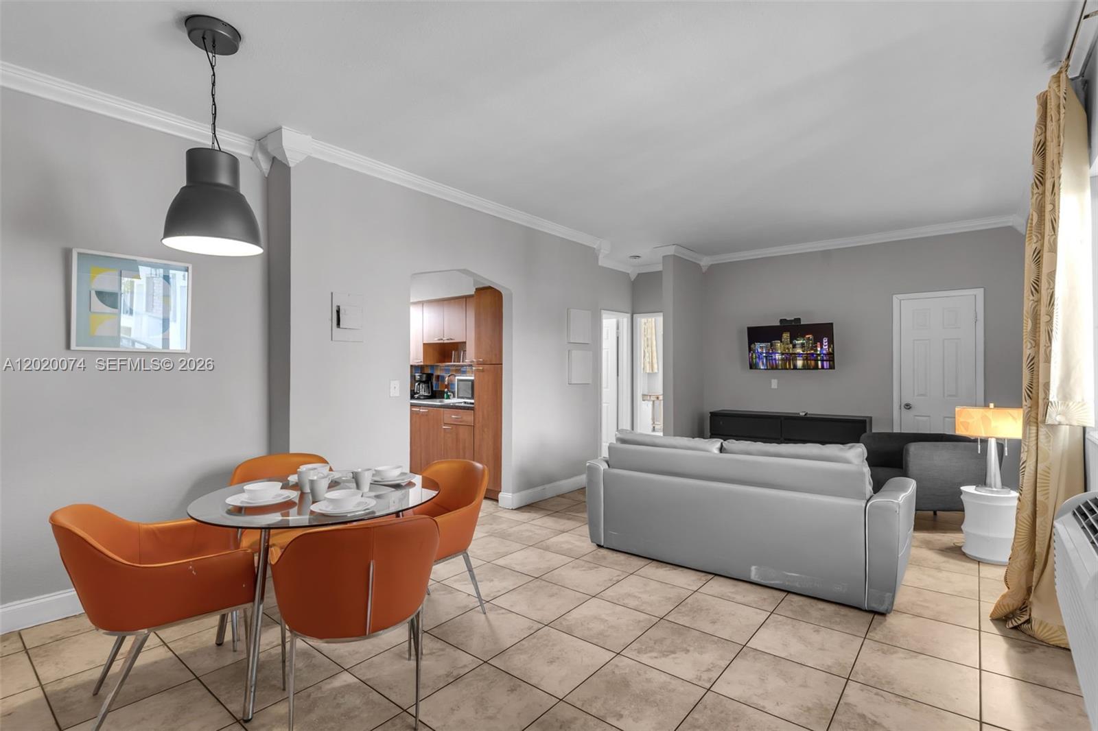 An open-concept living and dining area features tile flooring, orange chairs, and a grey sofa — 8100 Harding Ave # 503, Miami Beach FL 33141, MIAMI BEACH, FL