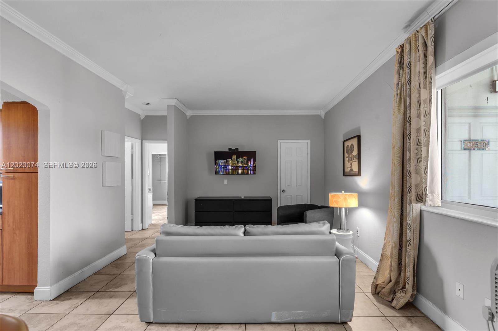 A living room features a gray sofa, a wall-mounted television, and tile flooring — 8100 Harding Ave # 503, Miami Beach FL 33141, MIAMI BEACH, FL