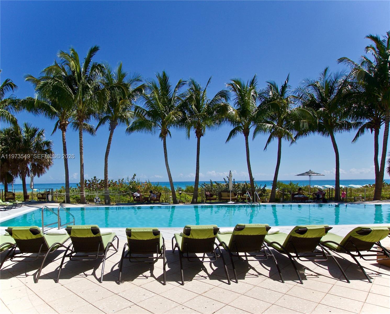 A swimming pool with lounge chairs sits in front of palm trees and the ocean — 6801 Collins Ave, Miami Beach FL 33141, MIAMI BEACH, FL