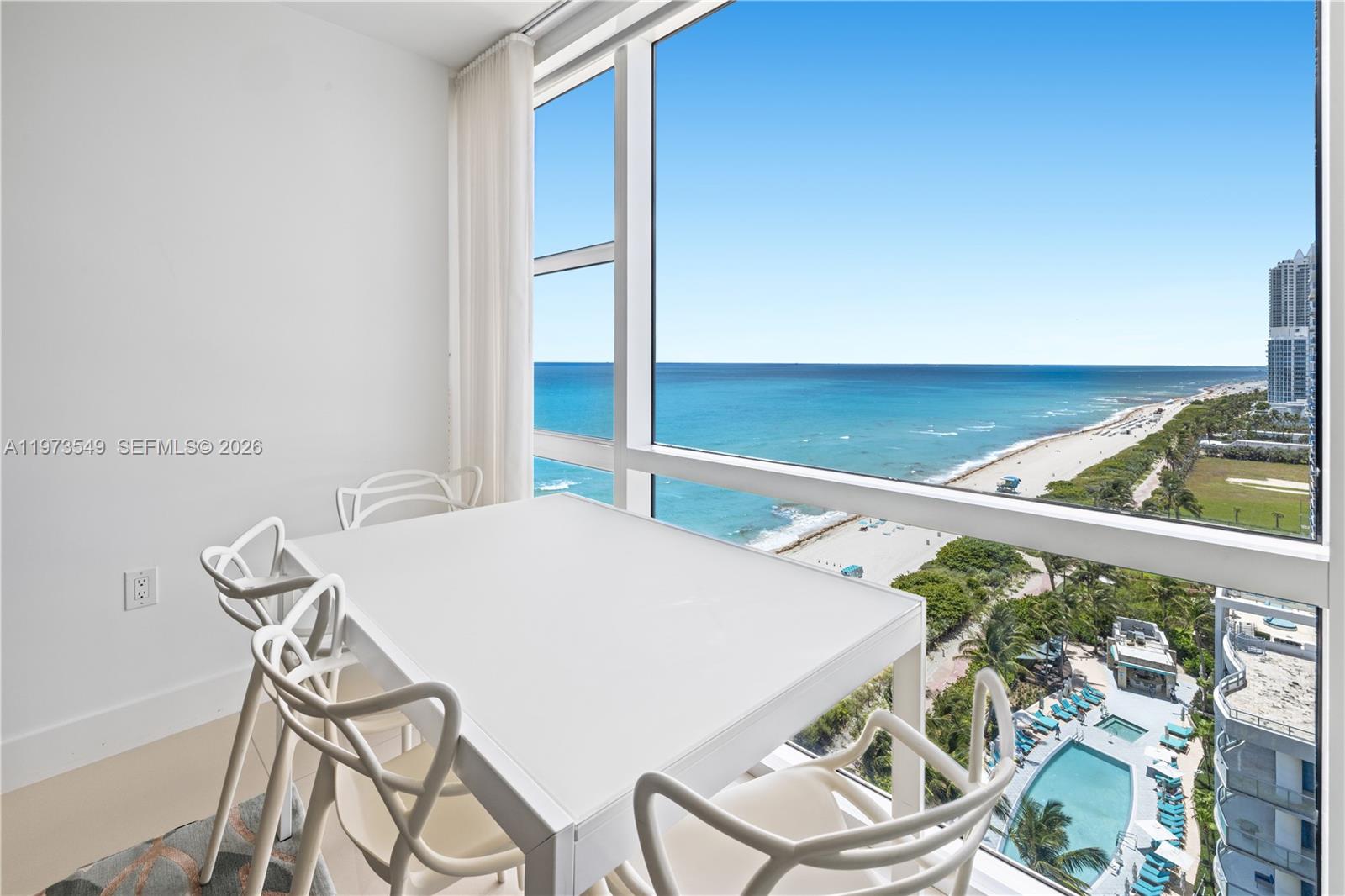 A dining area features a white table and chairs beside a large window overlooking the ocean — 6801 Collins Ave, Miami Beach FL 33141, MIAMI BEACH, FL